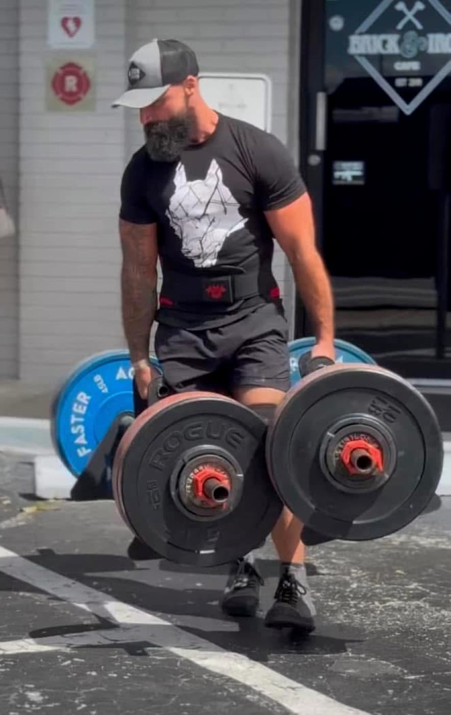 Sean carrying loaded dumbbells across a lot — the kind of working set clients film and send in.